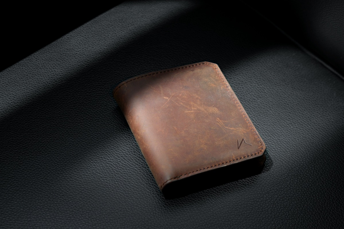 Brown leather wallet with essentials on wooden surface
